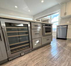 Kitchen featuring beverage cooler, stainless steel appliances, light wood-style flooring, gray cabinets, and backsplash