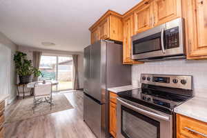 Kitchen with stainless steel appliances, light wood finished floors, tasteful backsplash, wood finish cabinetry, and a textured ceiling