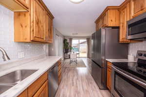 Kitchen featuring stainless steel appliances, decorative backsplash, light wood-type flooring, wood finish cabinetry, and a textured ceiling