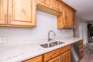 Kitchen featuring stainless steel dishwasher, wood finished floors, light stone counters, decorative backsplash, and a textured ceiling