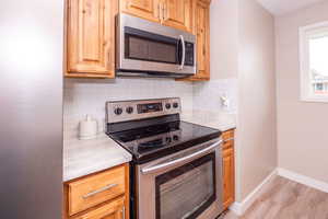 Kitchen with stainless steel appliances, decorative backsplash, light wood-style flooring, and light stone counters