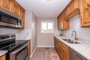 Kitchen featuring stainless steel appliances, wood finish cabinetry, light wood-type flooring, light stone countertops, and a textured ceiling