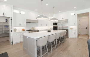 Kitchen with glass fronted cabinets, a kitchen bar, a center island, light wood finished floors, and built in appliances