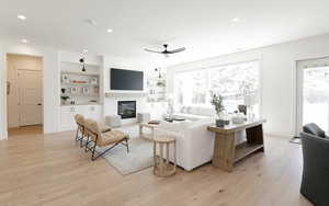 Living room with light wood-style floors, a large fireplace, recessed lighting, ceiling fan, and built in shelves