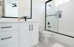 Bathroom featuring combined bath / shower with glass door, vanity, light tile patterned flooring, and a ceiling fan