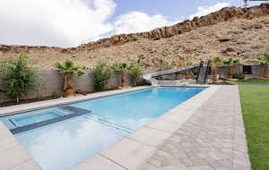 Integrated pool / spa with a water slide, a fenced backyard, and a patio area