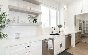 Kitchen with open shelves, white cabinets, tasteful backsplash, light stone counters, and stainless steel dishwasher