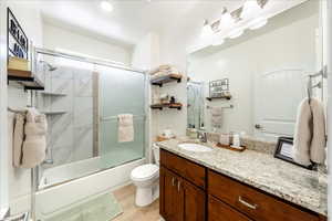 Full bathroom with vanity, bath / shower combo with glass door, and light wood finished floors