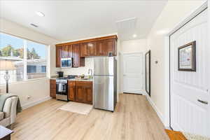 Kitchen featuring stainless steel appliances, light wood finished floors, light stone counters, recessed lighting, and open floor plan