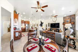 Dining area featuring ceiling fan, light flooring, a stone fireplace, and recessed lighting