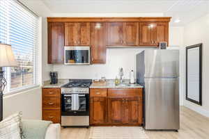 Kitchen featuring stainless steel appliances, wood finish cabinetry, light stone counters, and light wood-type flooring