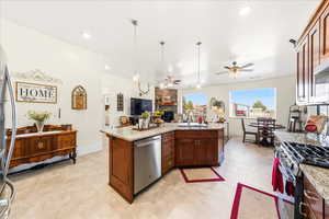 Kitchen with ceiling fan, light stone counters, open floor plan, decorative light fixtures, and stainless steel appliances