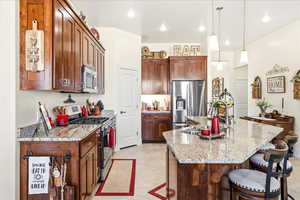 Kitchen featuring stainless steel appliances, light stone countertops, a center island with sink, and a breakfast bar area
