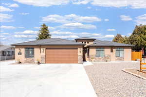 Prairie-style home with a garage, stucco siding, driveway, and stone siding