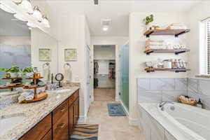 Bathroom with a spacious closet, double vanity, a garden tub, and a stall shower