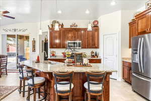 Kitchen with stainless steel appliances, light stone countertops, a kitchen bar, a center island with sink, and ceiling fan
