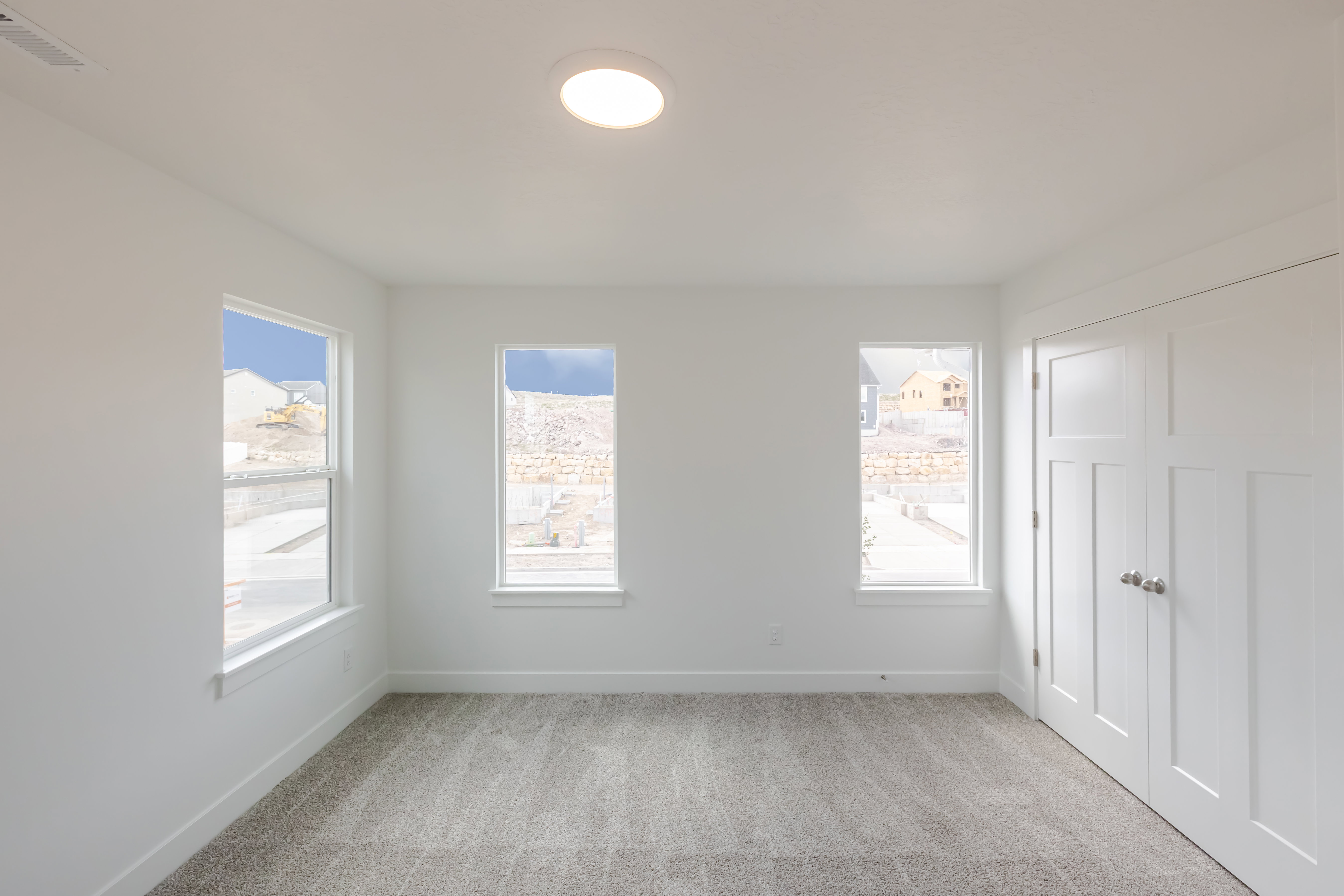 Bright interior space featuring three windows, a flush-mount ceiling light fixture, and neutral carpeting