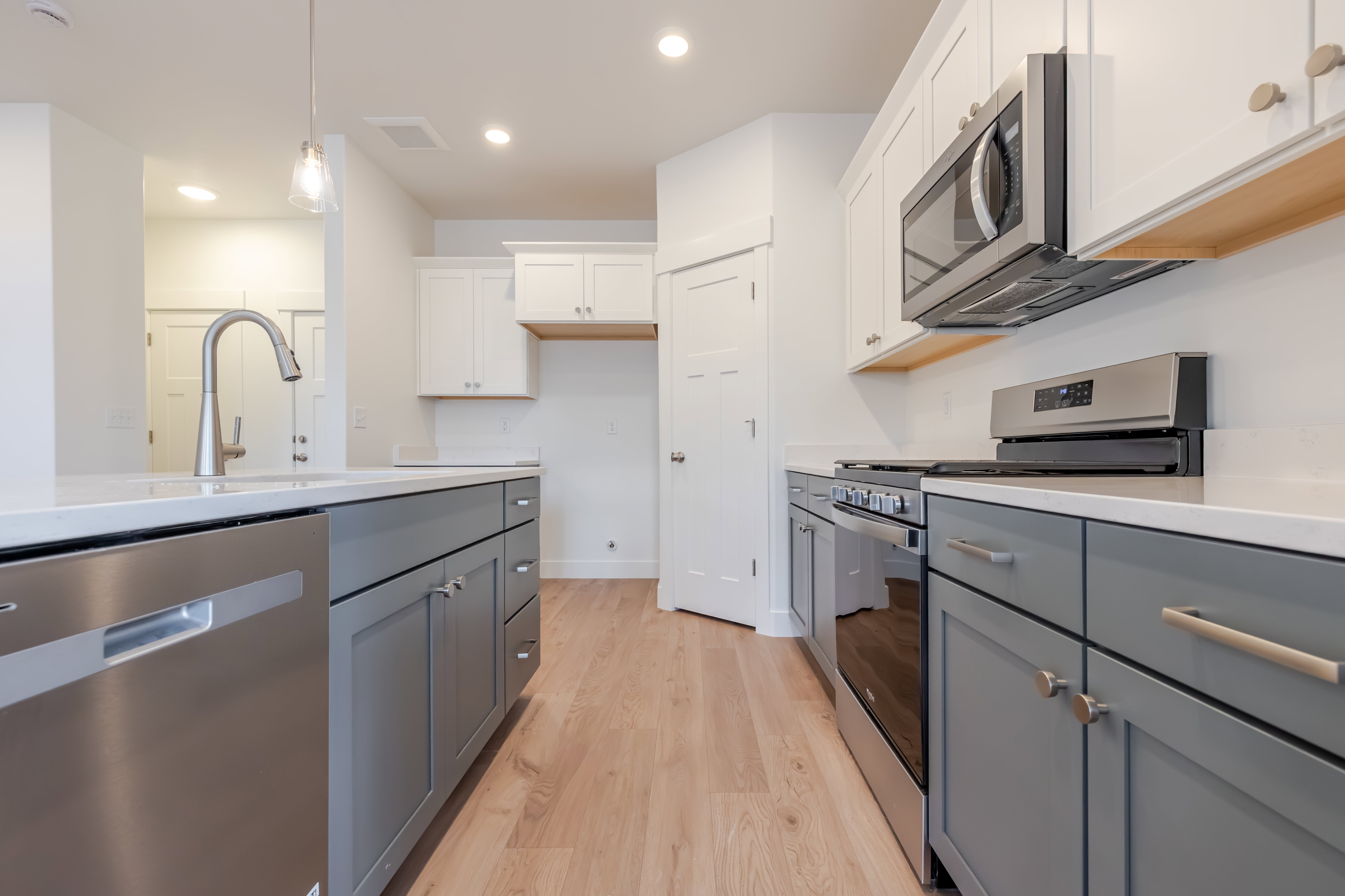 Contemporary kitchen featuring light wood-finish flooring, white countertops, stainless steel appliances, two-tone cabinetry, and recessed lighting