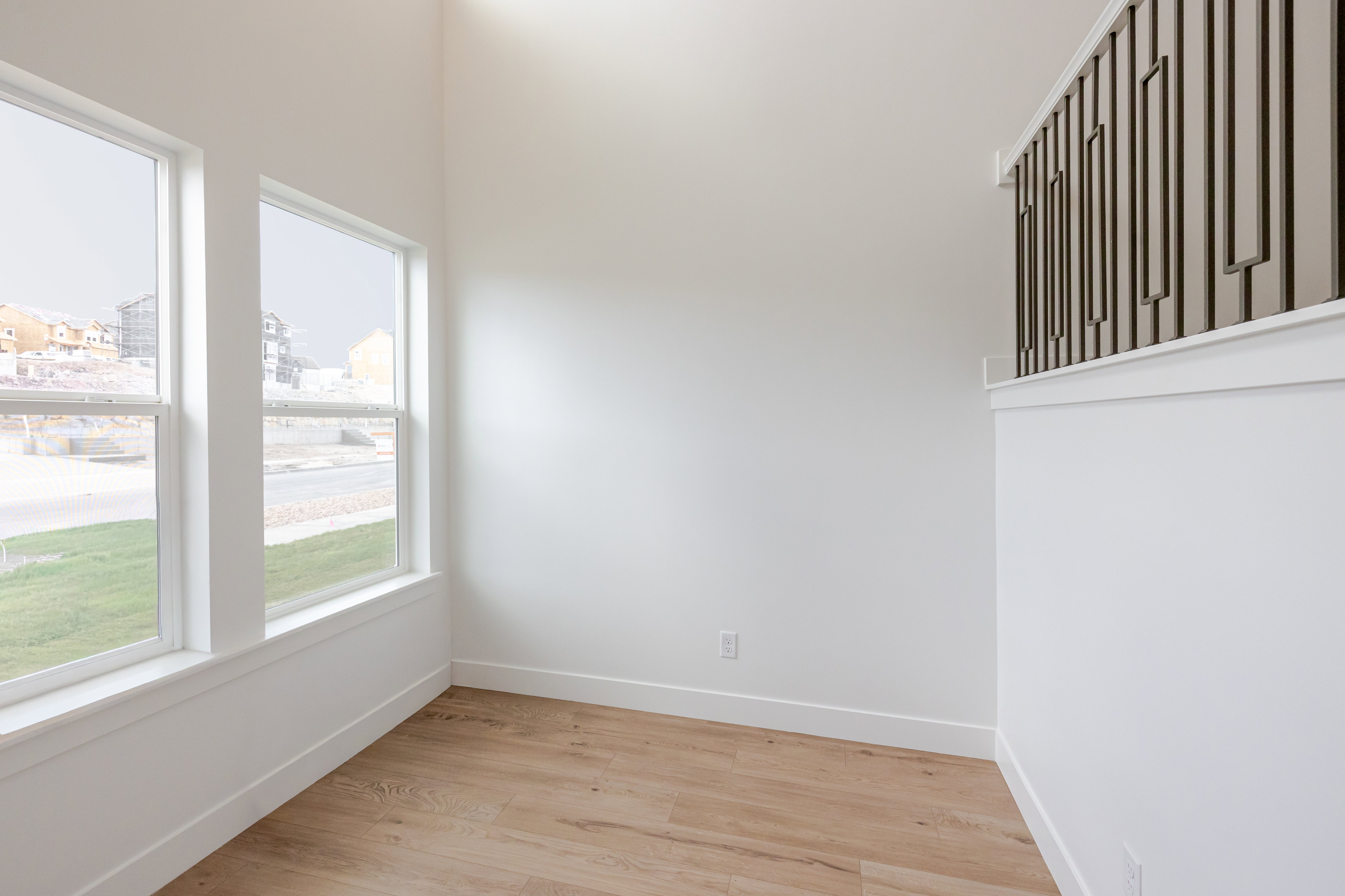 Bright interior space featuring three large windows, light wood-finish flooring, and a contemporary black metal and white wood railing