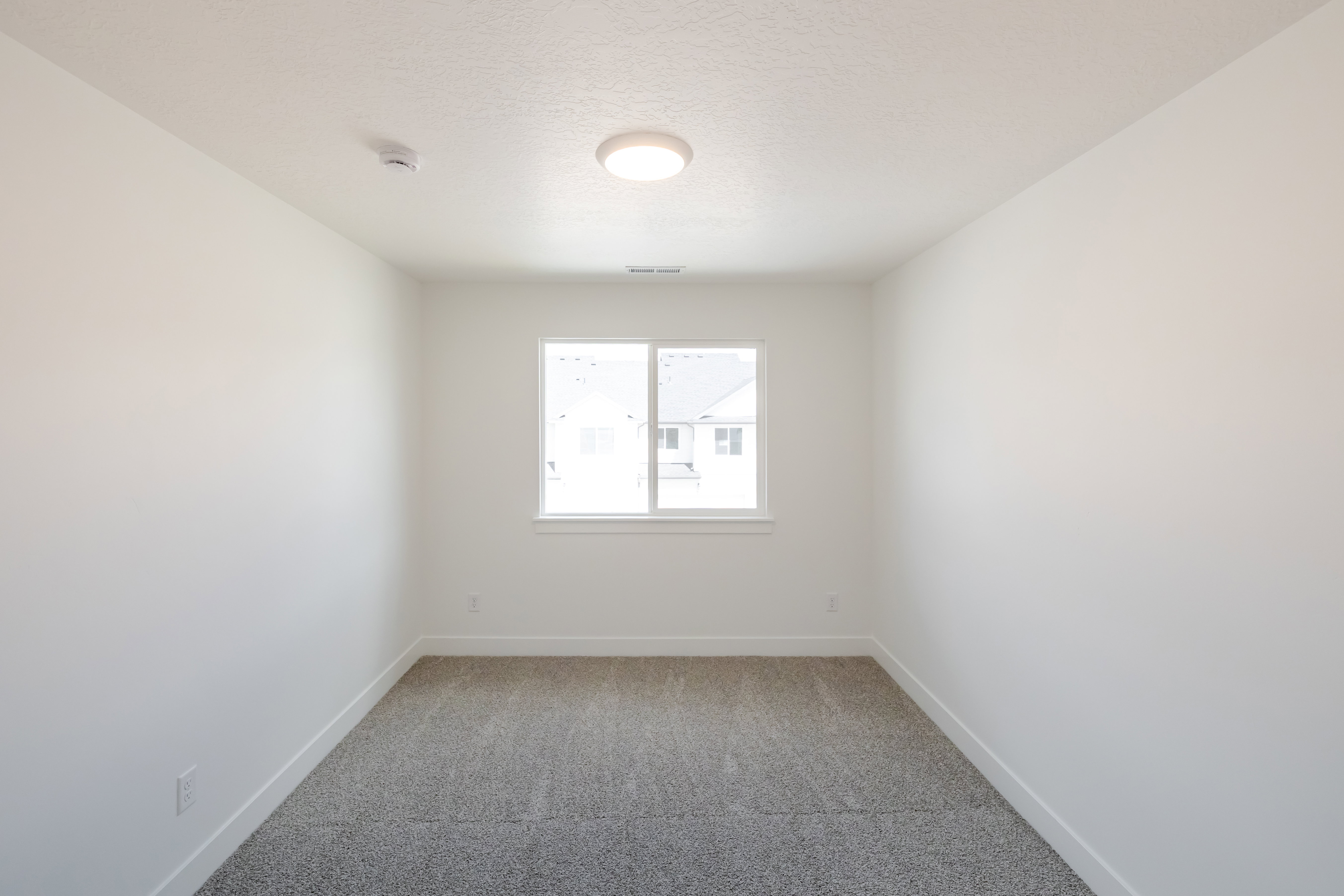 Bright interior space featuring a window with white trim, gray carpet flooring, white walls, white baseboards, and a flush-mount ceiling light fixture