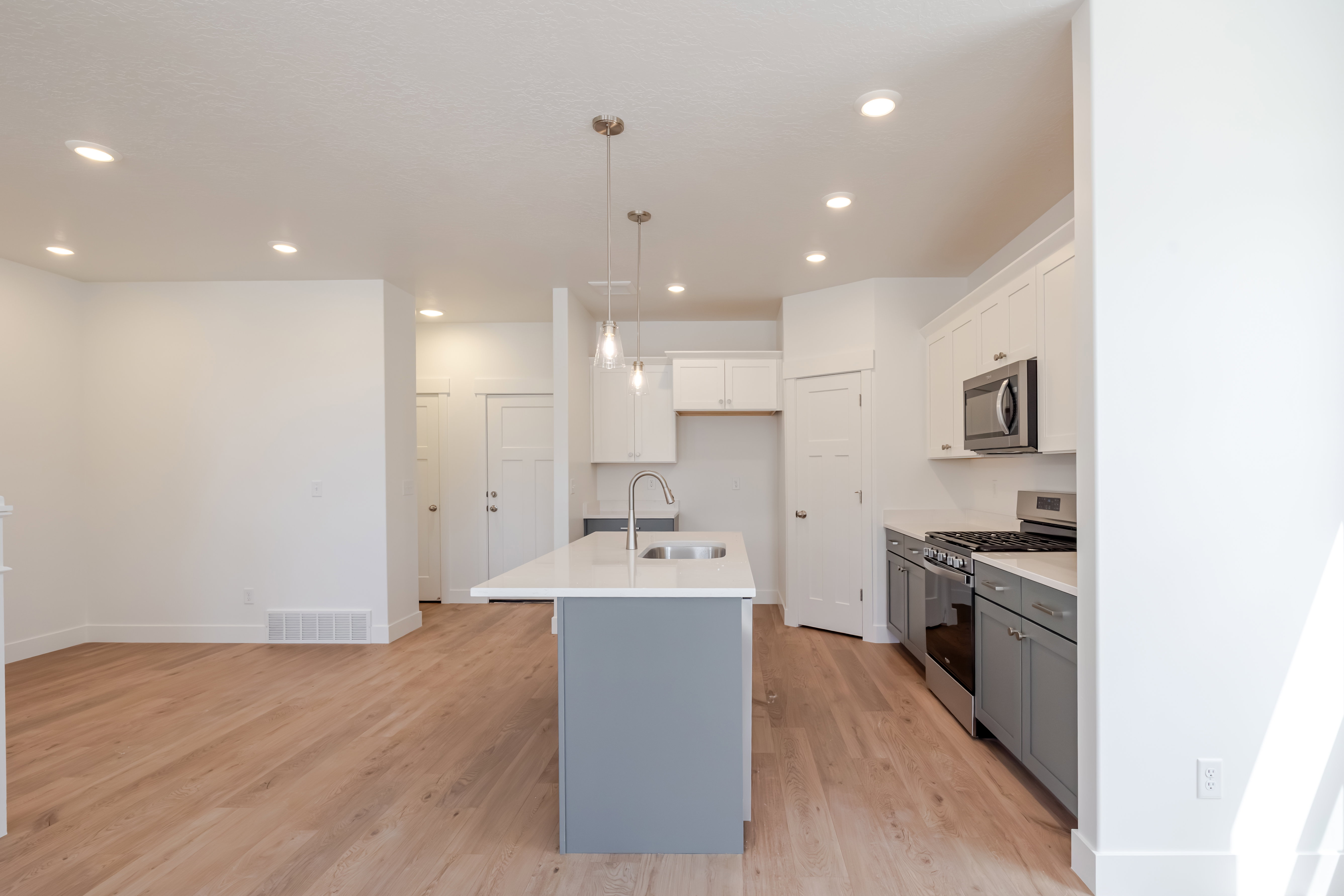 Open-concept kitchen featuring a center island with pendant lighting, light wood-finish flooring, white upper cabinetry, and gray lower cabinetry