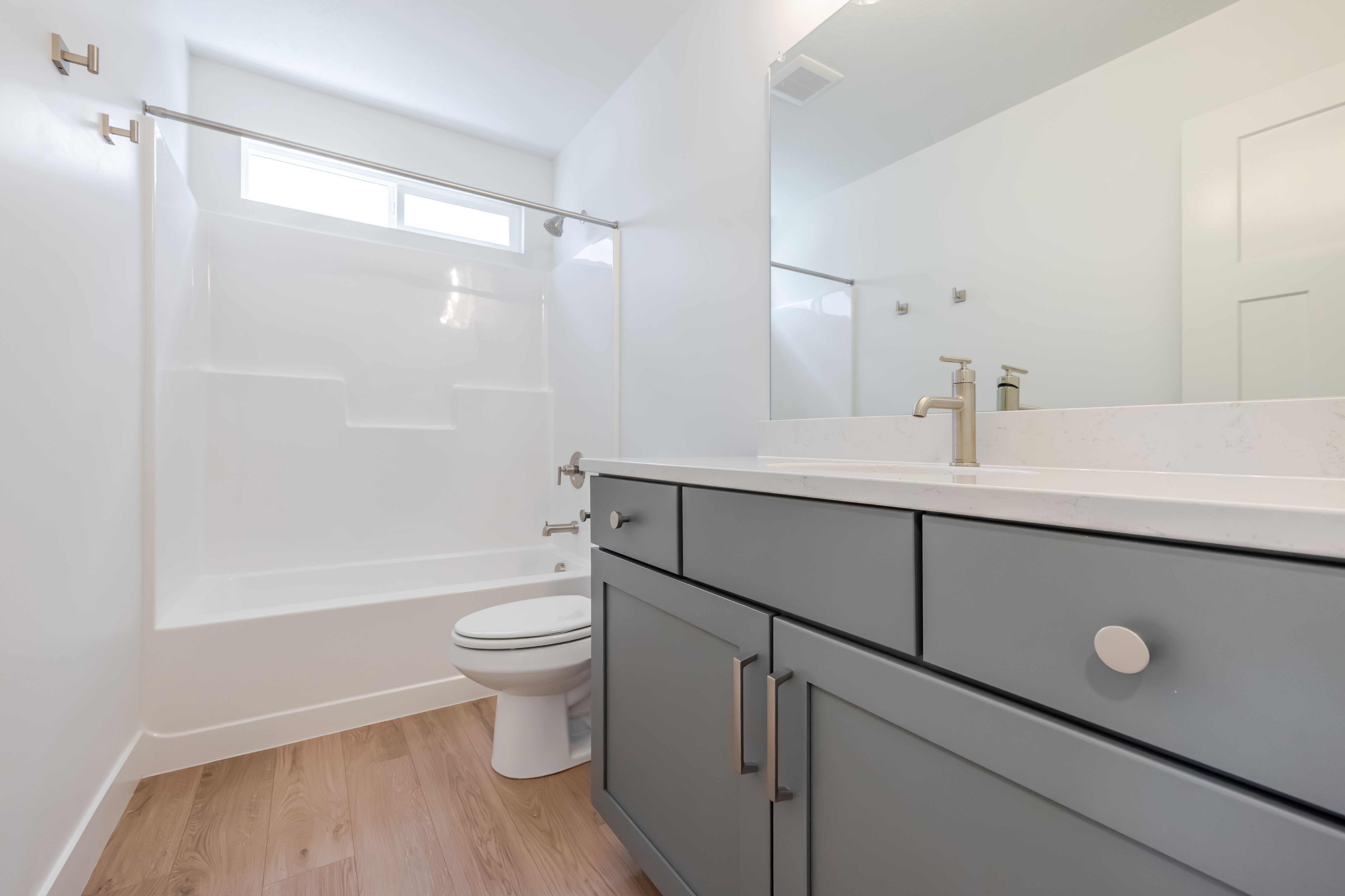 Bathroom vanity featuring a light gray finish with brushed nickel hardware, a white countertop with an integrated sink, and a brushed nickel faucet