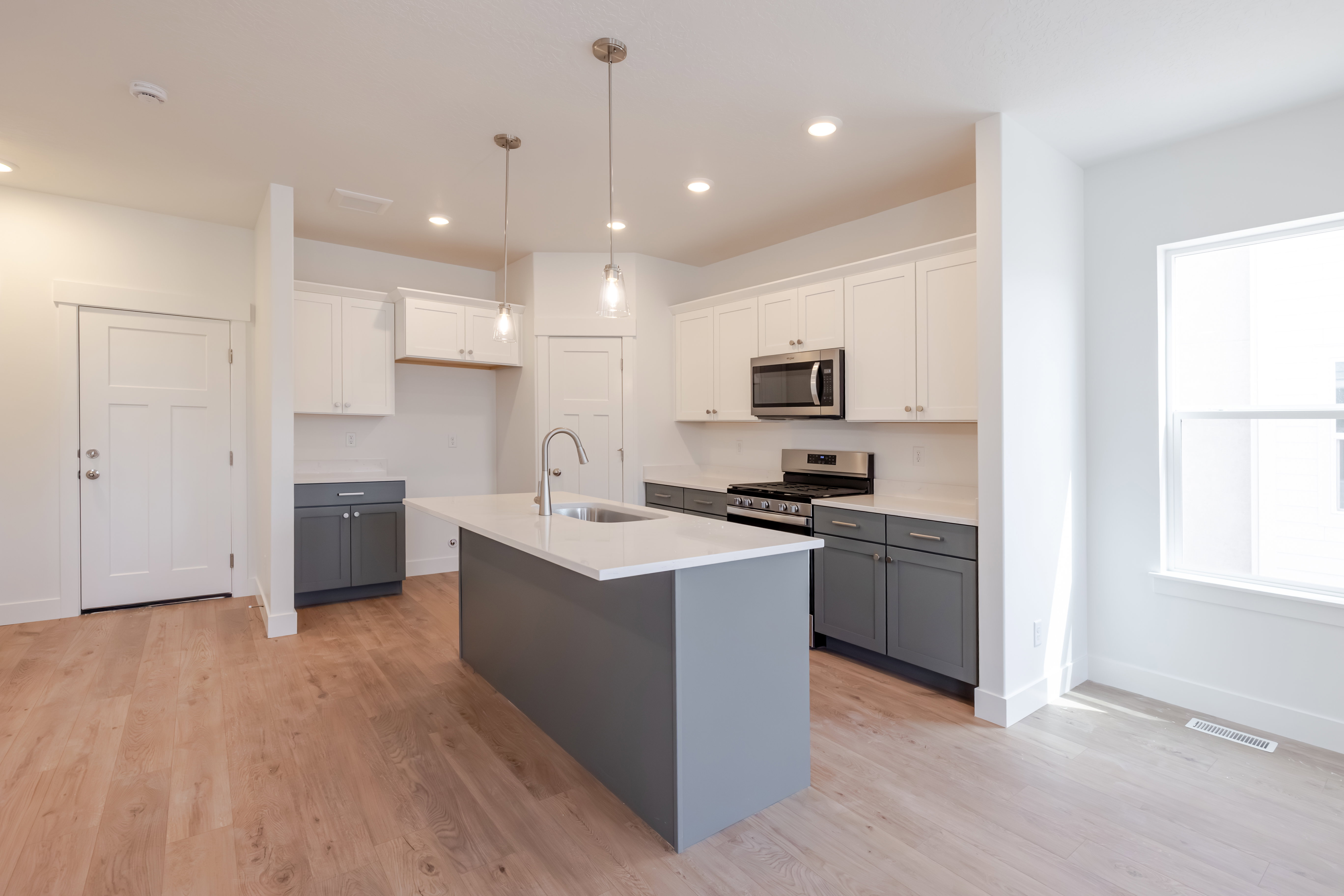 Modern kitchen featuring a central island with a sink, stainless steel appliances, two-tone cabinetry with white upper and grey lower units, and wood-finish flooring
