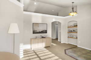 Unfurnished dining area with built in shelves, arched walkways, light colored carpet, and vaulted ceiling
