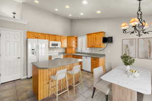 Kitchen with a center island, white appliances, a kitchen bar, hanging lights, and lofted ceiling
