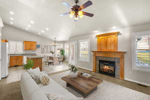 Living room with light carpet, healthy amount of natural light, a tile fireplace, ceiling fan, and vaulted ceiling