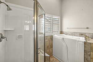 Bathroom with a stall shower, a garden tub, tile walls, and wainscoting