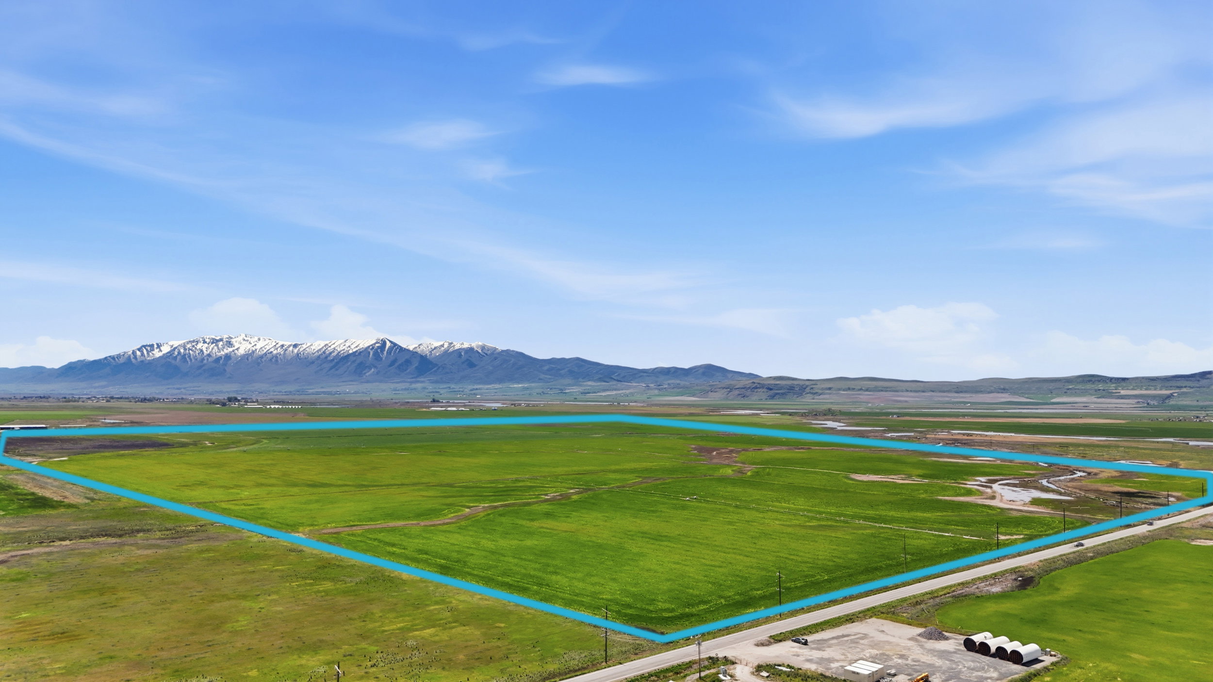 Expansive undeveloped land featuring a green field, a clear sky overhead, and distant mountains