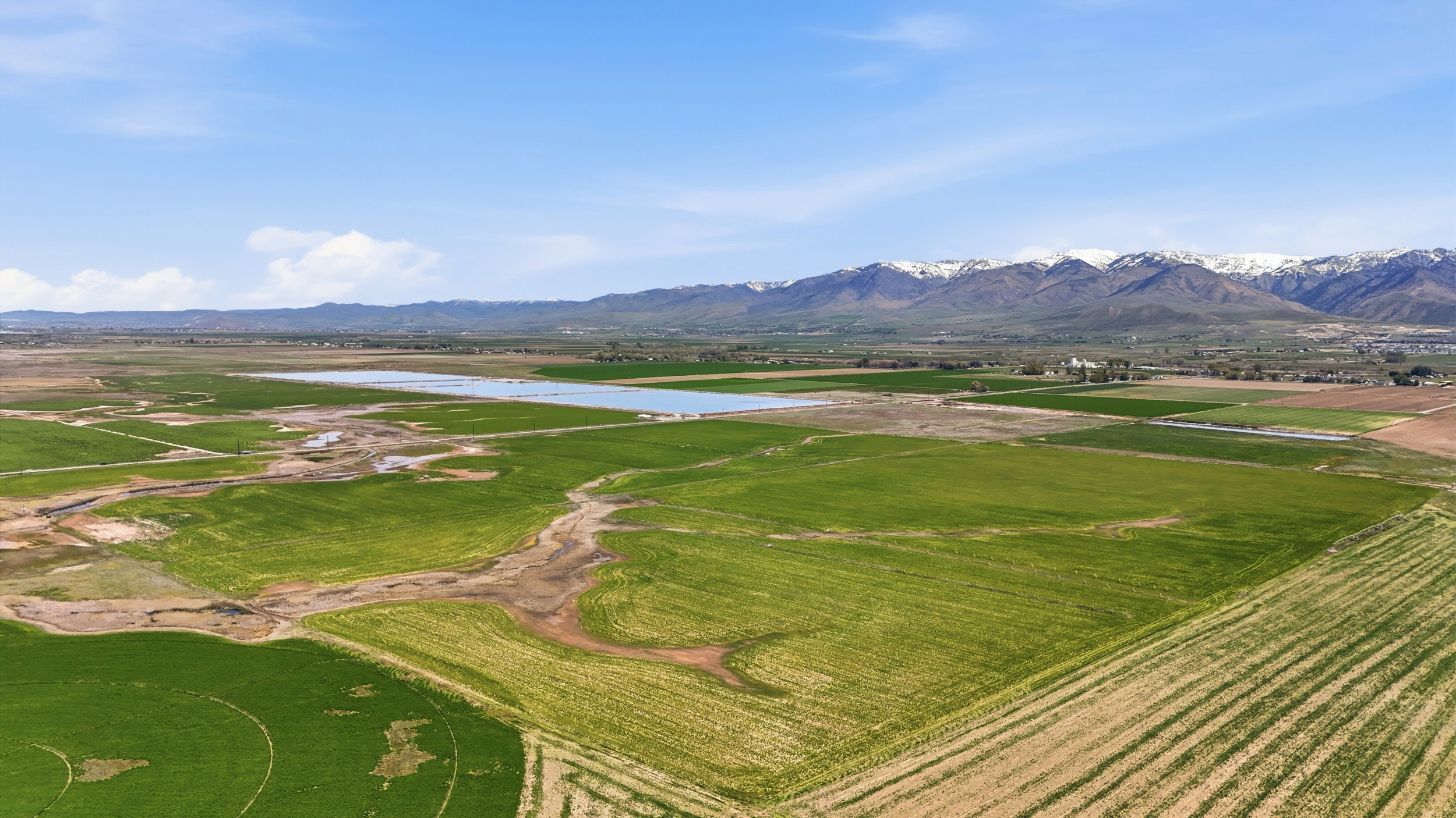 Expansive agricultural landscape featuring green fields, a body of water, and distant snow-capped mountains