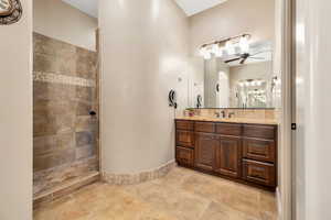 Bathroom with vanity, walk in shower, a ceiling fan, and light stone finish floors