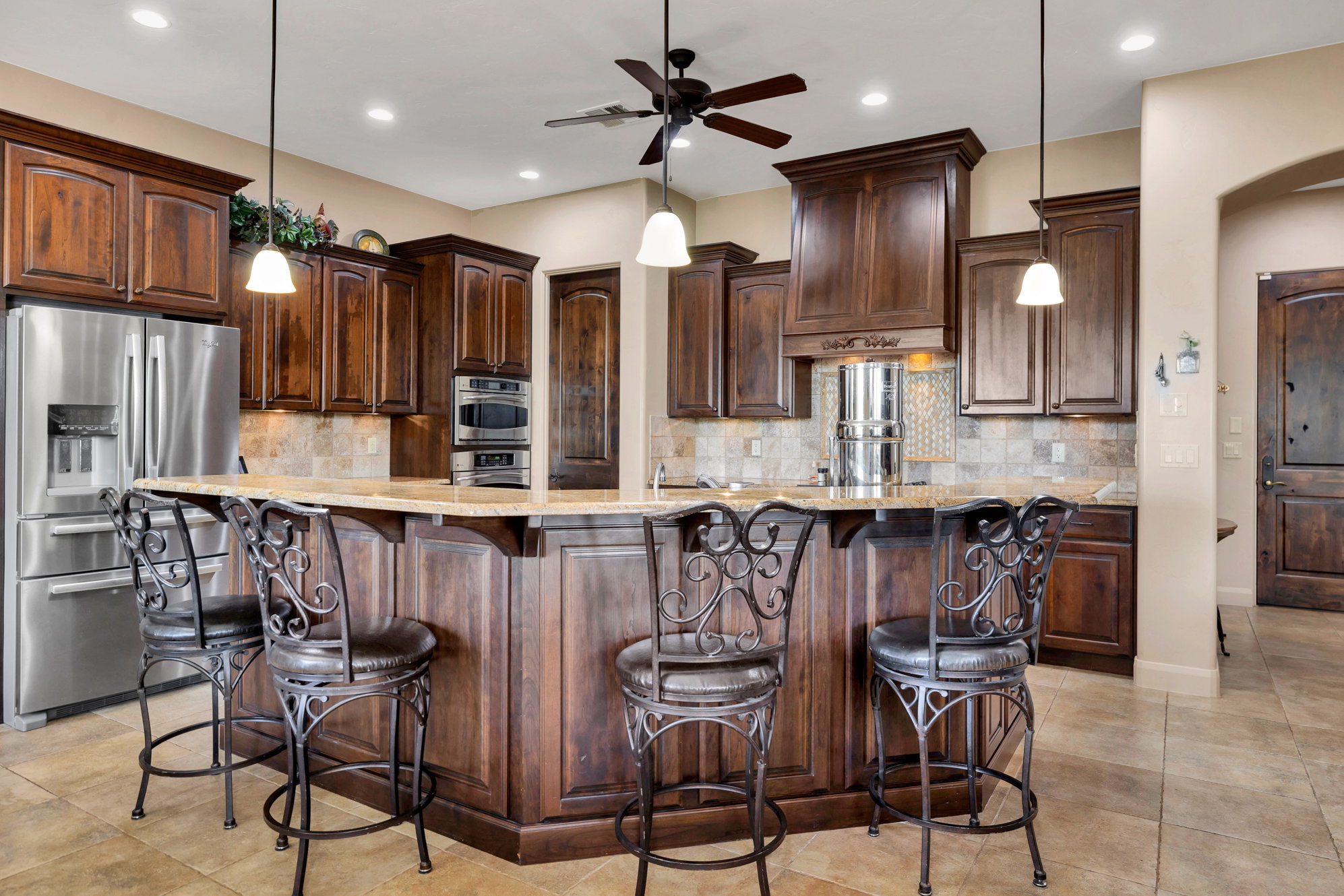 Kitchen with hanging light fixtures, stainless steel appliances, a kitchen bar, and light stone counters
