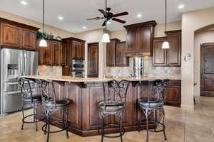 Kitchen with hanging light fixtures, stainless steel appliances, a kitchen bar, and light stone counters
