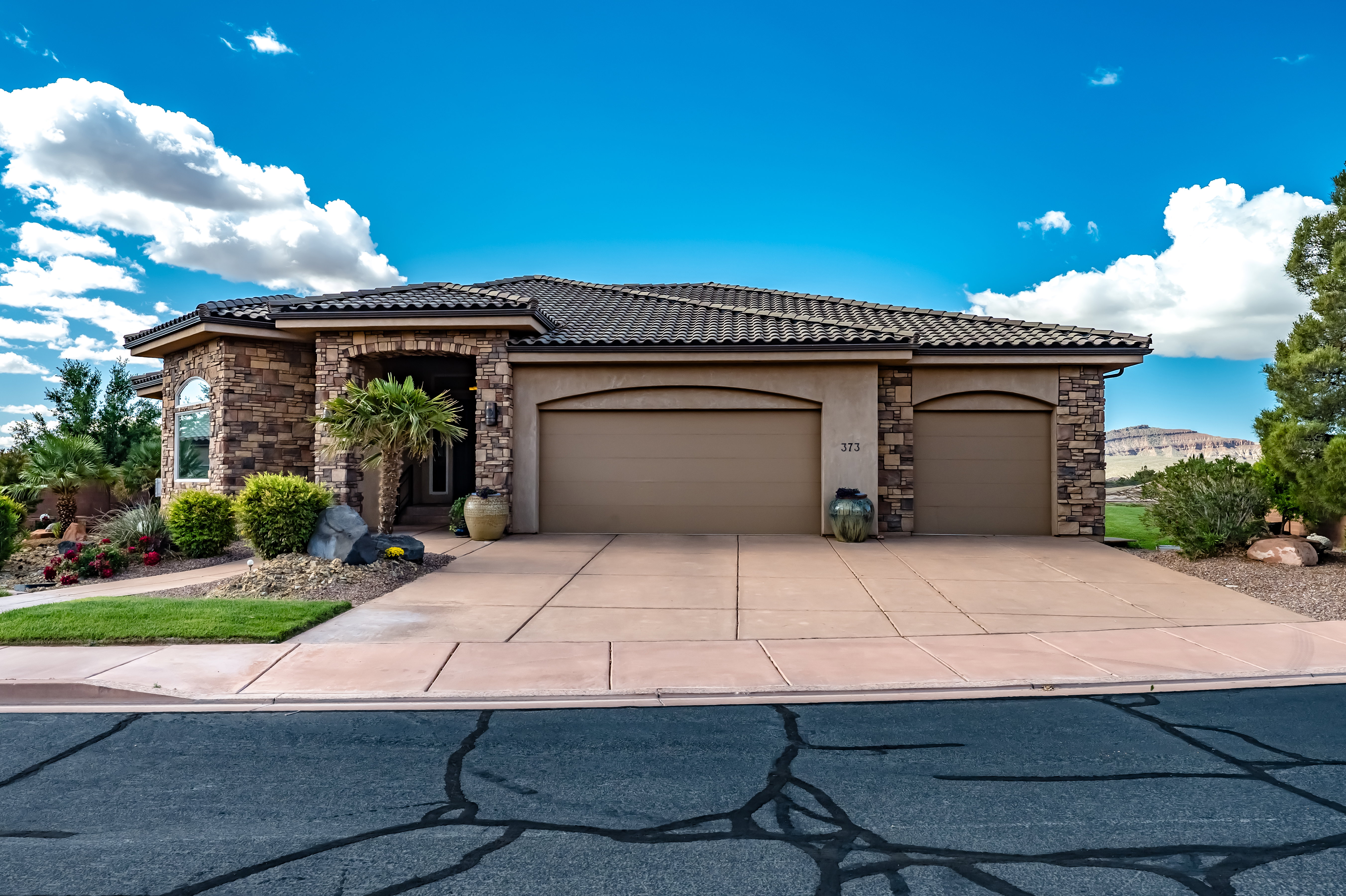 View of front of property featuring stone siding, a tiled roof, stucco siding, driveway, and a garage