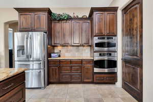 Kitchen featuring stainless steel appliances, dark wood finish cabinetry, light stone counters, tasteful backsplash, and arched walkways