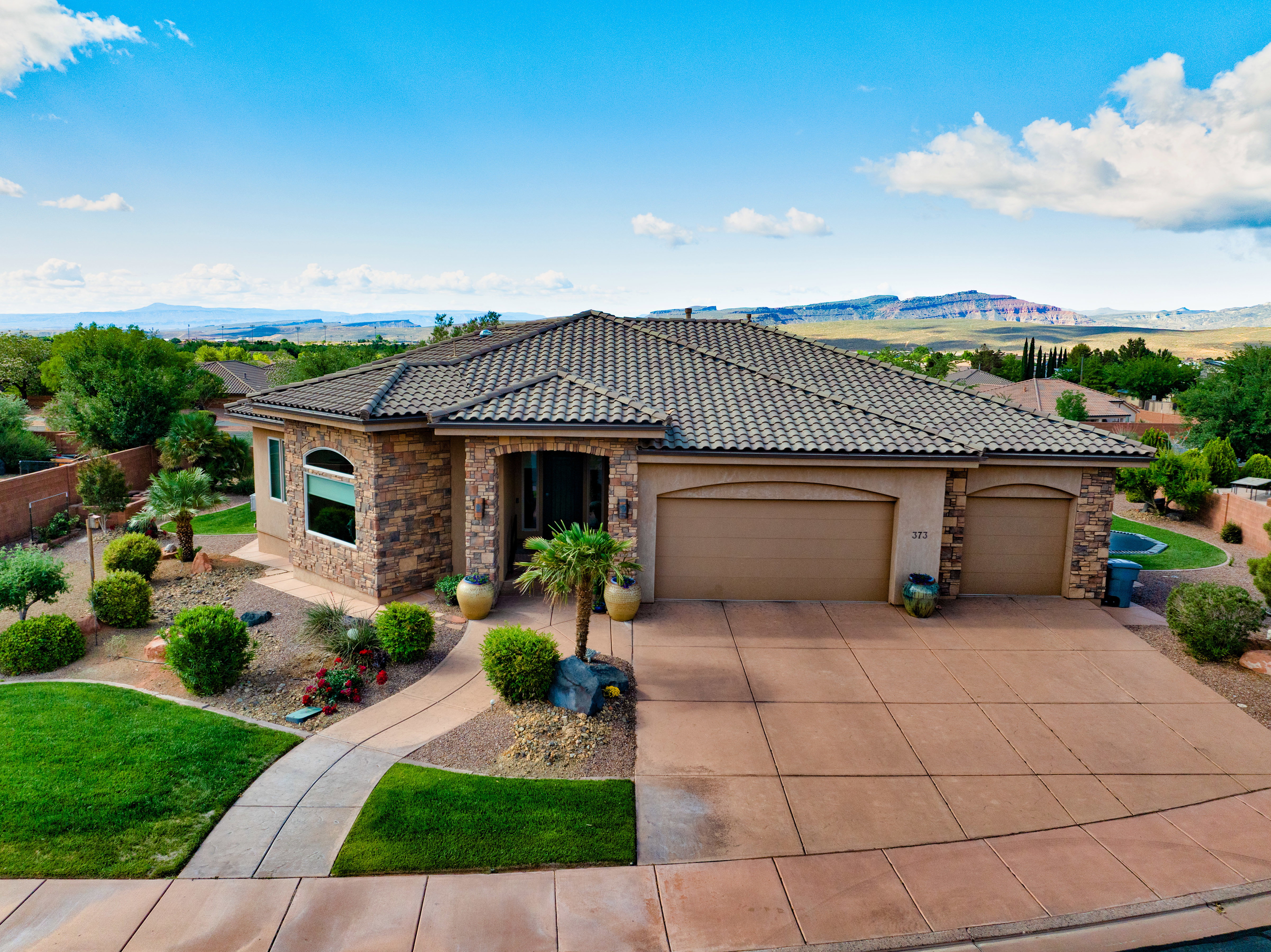 View of front of property featuring stone siding, an attached garage, stucco siding, and a tiled roof