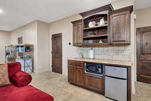 Kitchen with freestanding refrigerator, open shelves, dark wood finish cabinetry, and backsplash