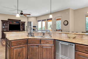 Kitchen with open floor plan, dishwasher, pendant lighting, light stone countertops, and a ceiling fan