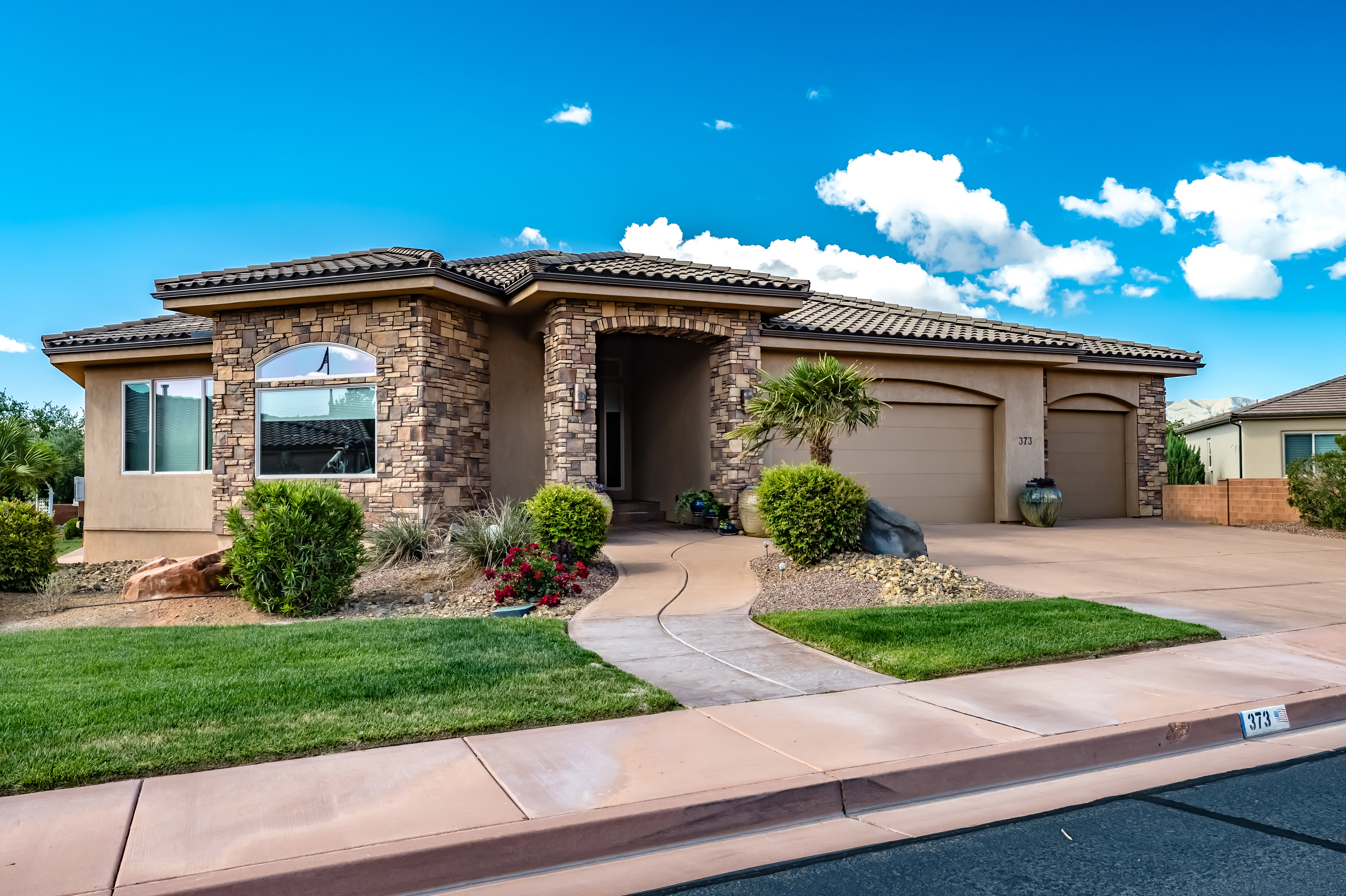 Mediterranean / spanish home featuring stucco siding, a tiled roof, an attached garage, concrete driveway, and stone siding