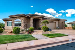 Mediterranean / spanish home featuring stucco siding, a tiled roof, an attached garage, concrete driveway, and stone siding