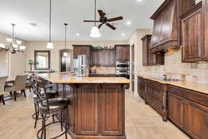 Kitchen featuring a kitchen bar, light stone countertops, stainless steel appliances, dark wood finish cabinetry, and a ceiling fan