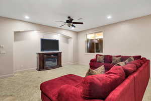 Living room featuring light carpet, a ceiling fan, a glass covered fireplace, and recessed lighting