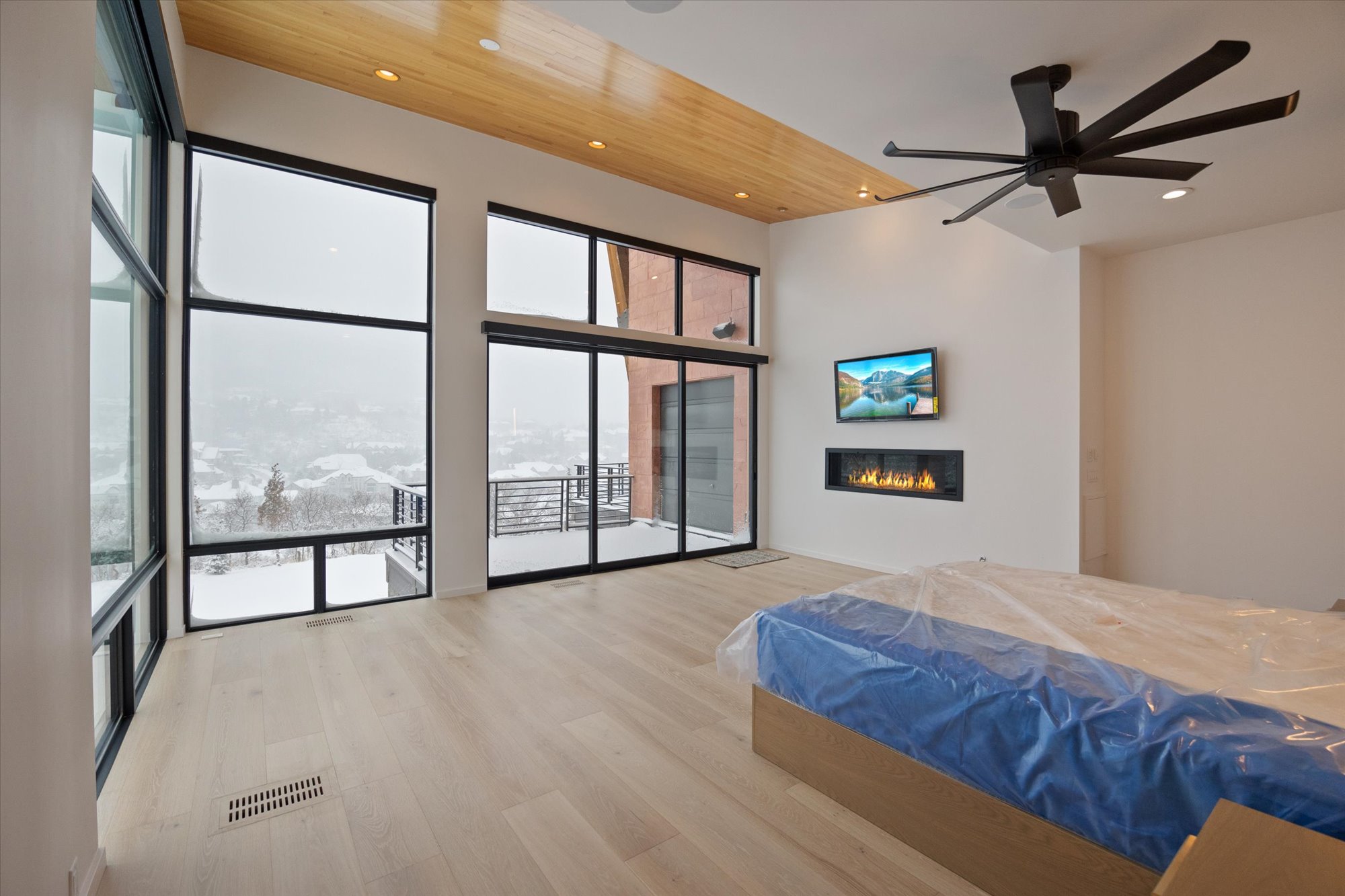 Bedroom featuring a glass covered fireplace, light wood-type flooring, ceiling fan, a high ceiling, and recessed lighting