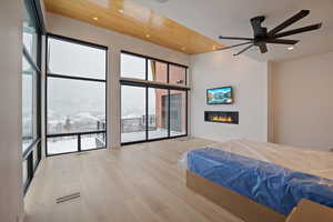 Bedroom featuring a glass covered fireplace, light wood-type flooring, ceiling fan, a high ceiling, and recessed lighting