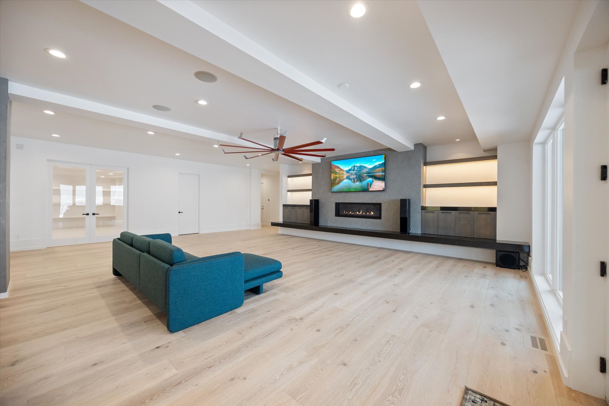 Unfurnished living room with beamed ceiling, light wood-style flooring, a glass covered fireplace, recessed lighting, and french doors