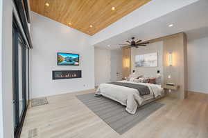 Bedroom with a glass covered fireplace, light wood finished floors, wooden ceiling, recessed lighting, and ceiling fan