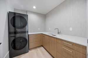 Laundry area featuring light wood-type flooring, stacked washer and clothes dryer, recessed lighting, and cabinet space